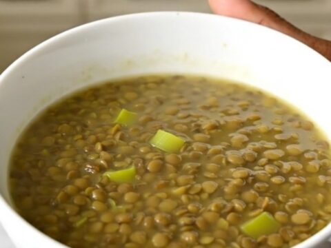 A rustic green lentil and leek soup in a white bowl on a wooden table.
