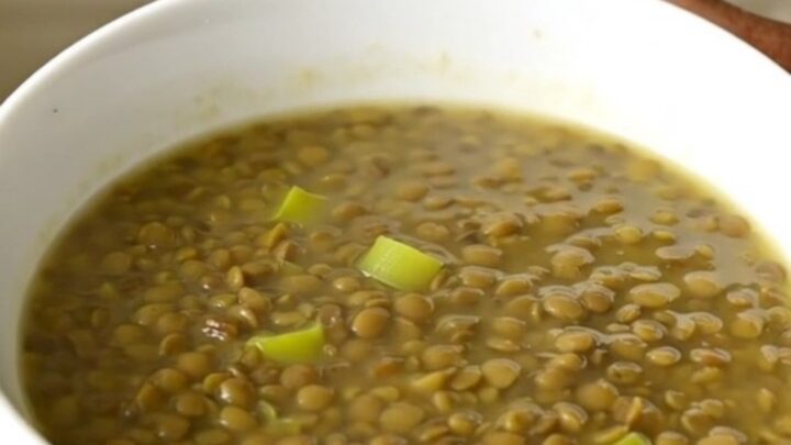 A rustic green lentil and leek soup in a white bowl on a wooden table.