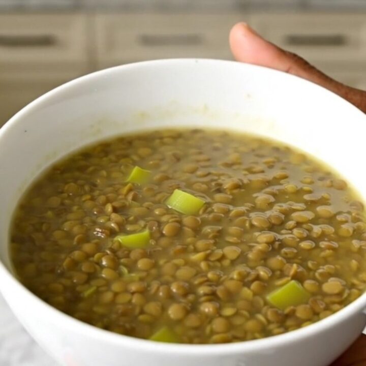A rustic green lentil and leek soup in a white bowl on a wooden table.