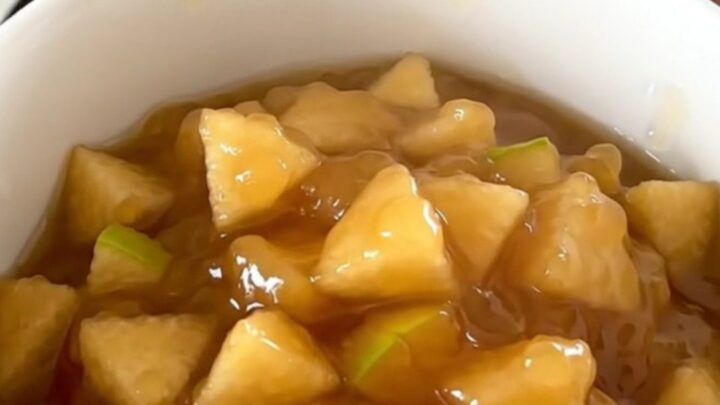 A white ceramic bowl filled with warm, glossy apple and pear compote, showing soft fruit pieces and syrup.