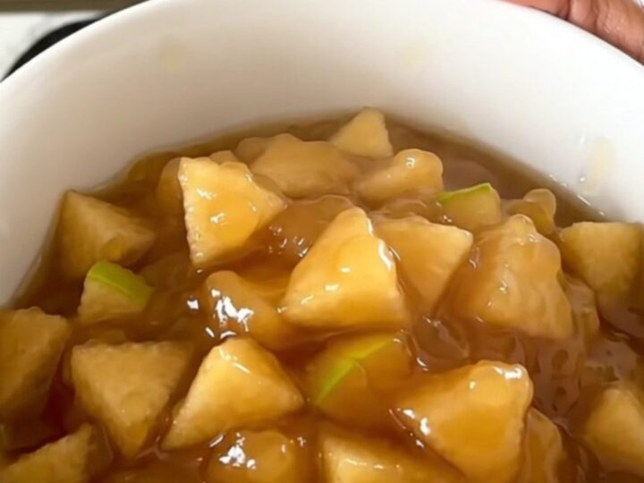 A white ceramic bowl filled with warm, glossy apple and pear compote, showing soft fruit pieces and syrup.