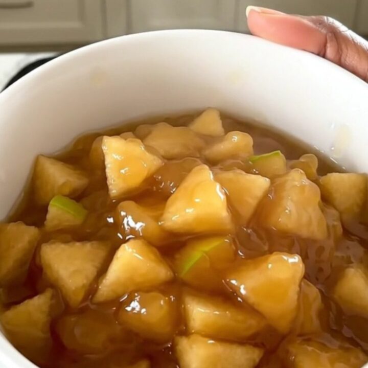 A white ceramic bowl filled with warm, glossy apple and pear compote, showing soft fruit pieces and syrup.