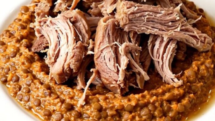 A close-up of tender, shredded pork shoulder served with a creamy red lentil and carrot puree on a white plate.