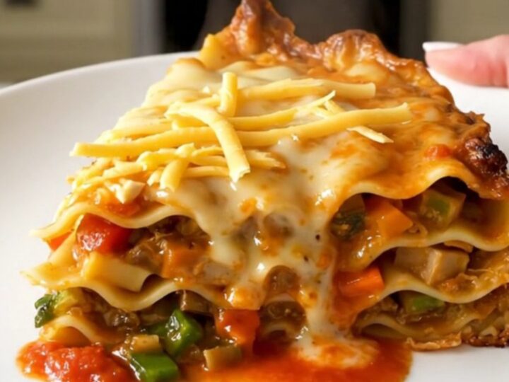 A steaming, glossy slice of autumn vegetable lasagna served on a plain white plate.