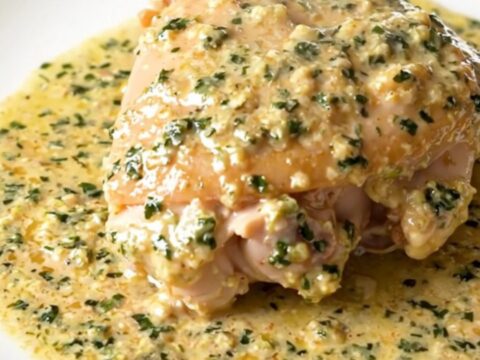 A close-up of tender chicken thighs in a glossy, creamy tarragon sauce served on a white plate.