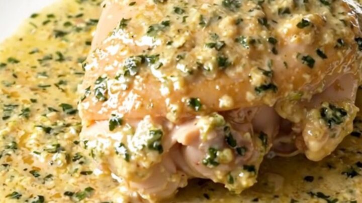 A close-up of tender chicken thighs in a glossy, creamy tarragon sauce served on a white plate.