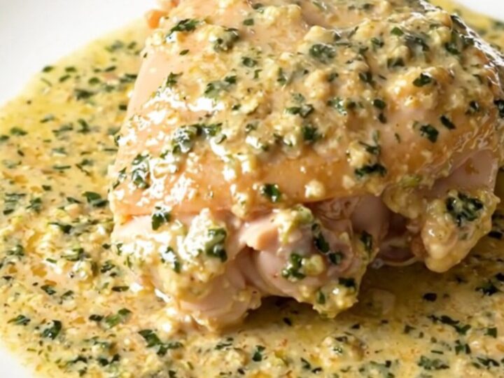 A close-up of tender chicken thighs in a glossy, creamy tarragon sauce served on a white plate.