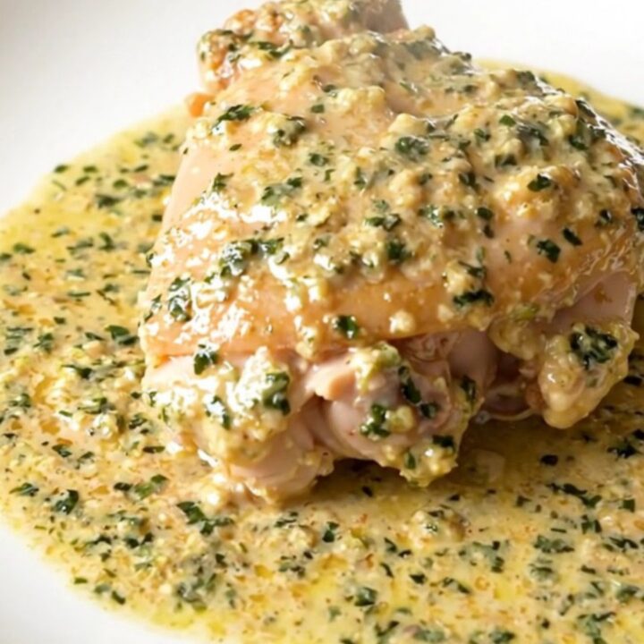 A close-up of tender chicken thighs in a glossy, creamy tarragon sauce served on a white plate.
