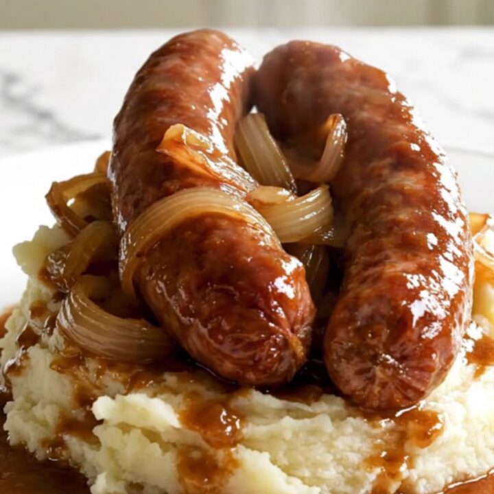 A black slow cooker filled with raw Toulouse sausages and sliced sweet onions on a white speckled quartz countertop.