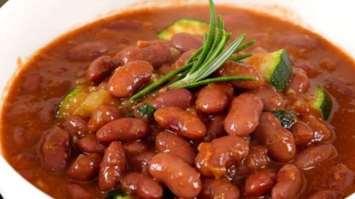 A rustic bowl of slow-cooked red kidney beans, zucchini, and tomato stew, steaming and glistening.