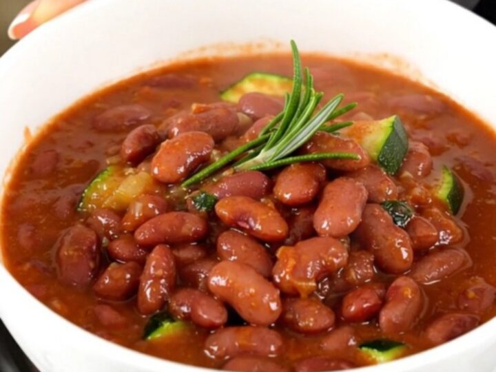 A rustic bowl of slow-cooked red kidney beans, zucchini, and tomato stew, steaming and glistening.
