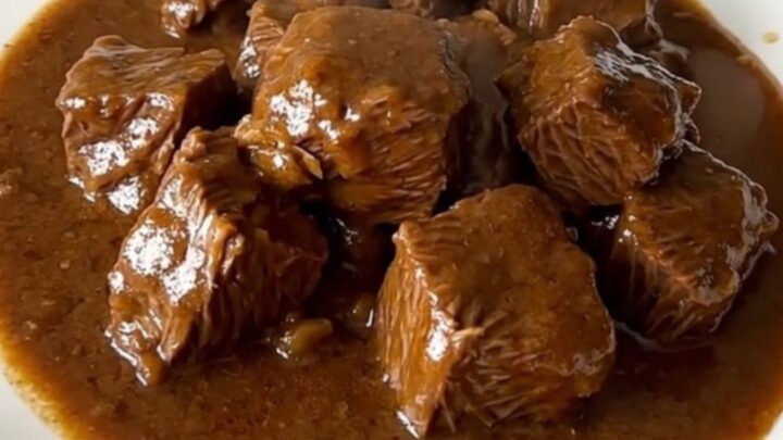 A close-up of a bowl of rich, dark beef carbonnade with tender beef chunks and thick gravy.