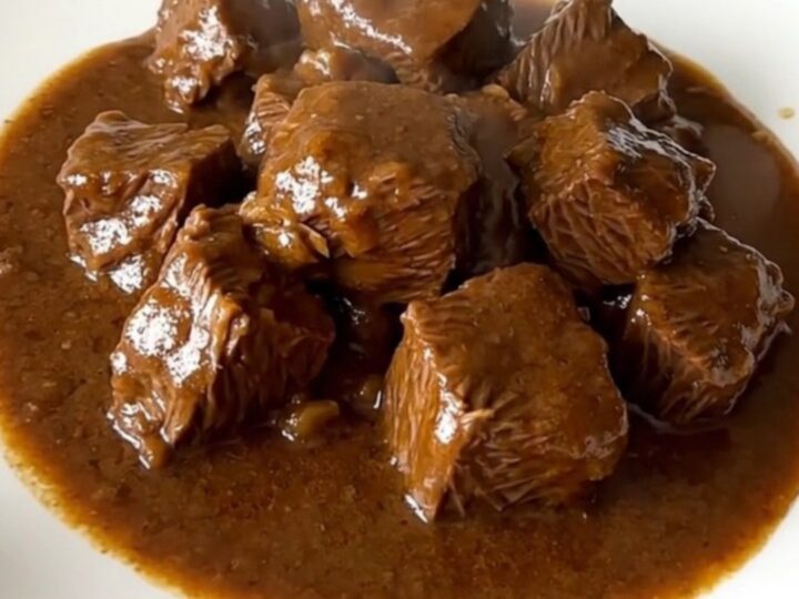 A close-up of a bowl of rich, dark beef carbonnade with tender beef chunks and thick gravy.