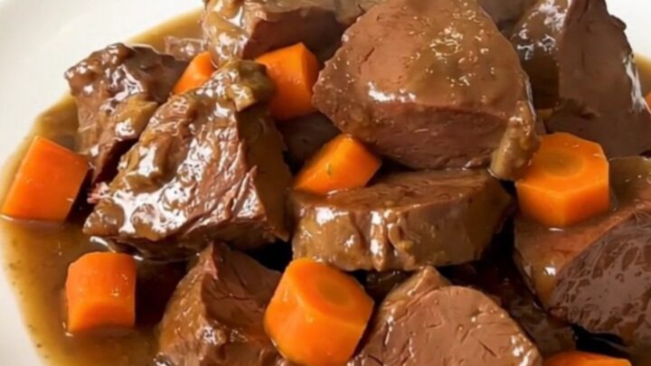 A close-up of a bowl of slow-cooked, tender beer-braised veal stew with carrots and onions in a rich, glossy brown sauce.