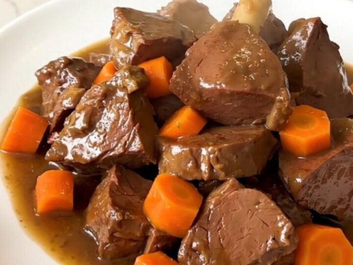 A close-up of a bowl of slow-cooked, tender beer-braised veal stew with carrots and onions in a rich, glossy brown sauce.