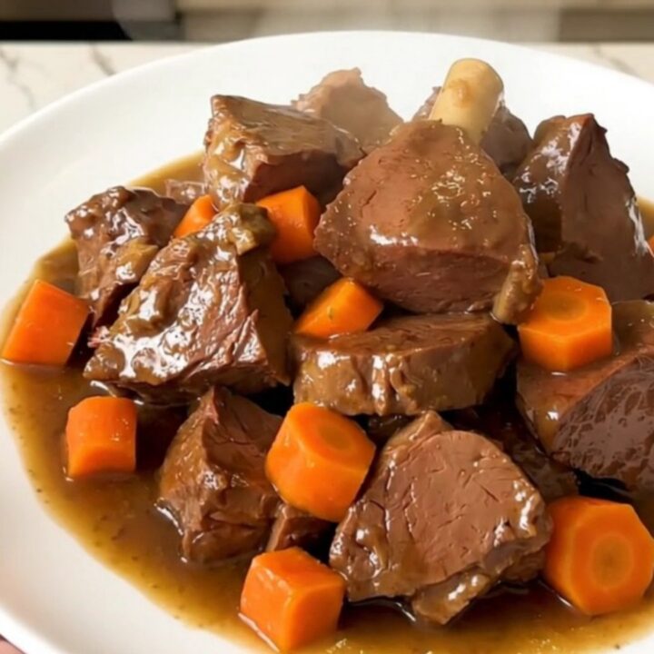 A close-up of a bowl of slow-cooked, tender beer-braised veal stew with carrots and onions in a rich, glossy brown sauce.