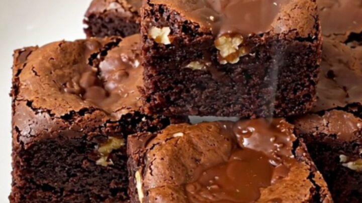 A close-up of a warm, fudgy walnut brownie square on a white plate, showing a dense and glossy texture.
