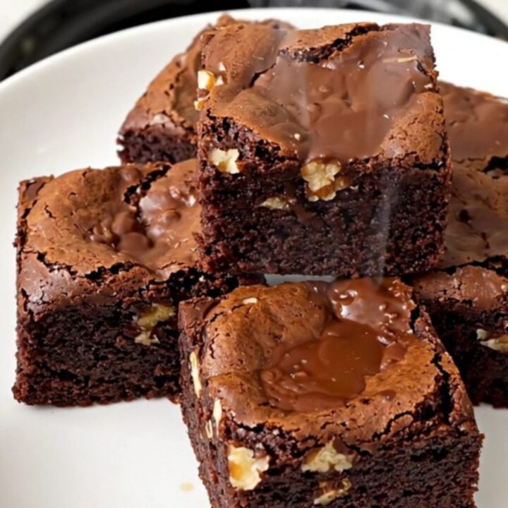 A close-up of a warm, fudgy walnut brownie square on a white plate, showing a dense and glossy texture.