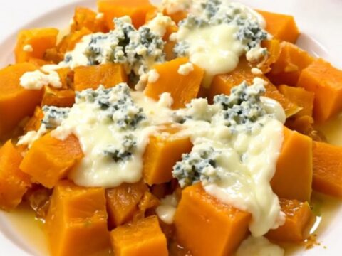 A top-down view of a black slow cooker filled with cooked butternut squash cubes and sliced onions.