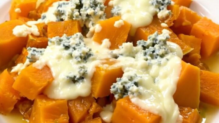 A top-down view of a black slow cooker filled with cooked butternut squash cubes and sliced onions.