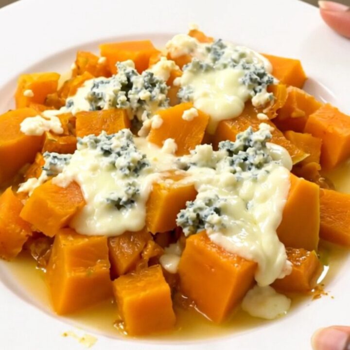 A top-down view of a black slow cooker filled with cooked butternut squash cubes and sliced onions.