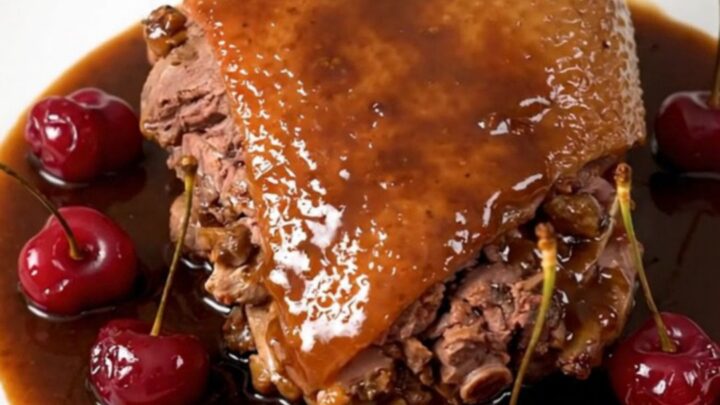 Slow-cooked duck legs with a glossy cherry and port wine reduction served on a white plate.