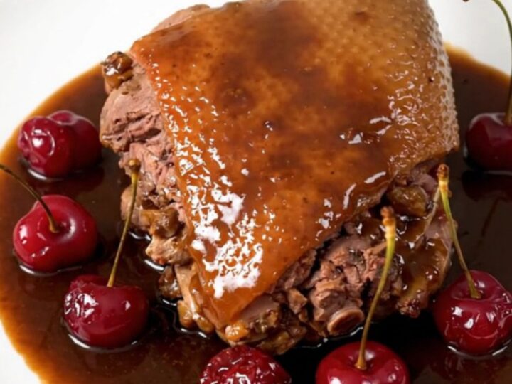 Slow-cooked duck legs with a glossy cherry and port wine reduction served on a white plate.