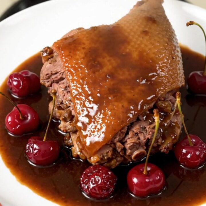Slow-cooked duck legs with a glossy cherry and port wine reduction served on a white plate.
