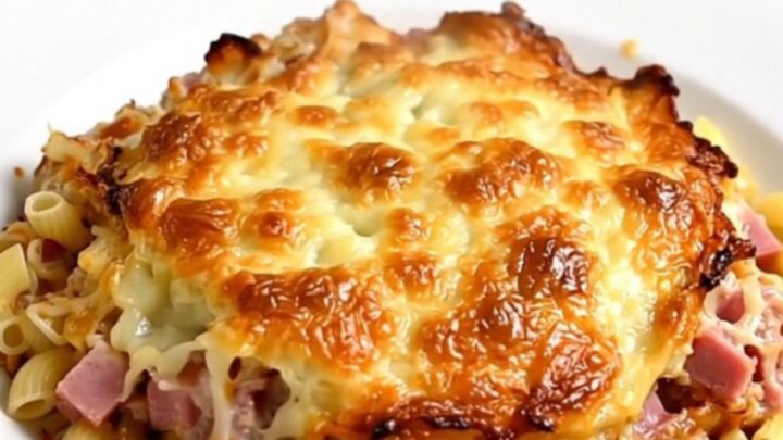 A close-up of a steaming portion of creamy elbow pasta with diced ham in a rich cheese sauce.