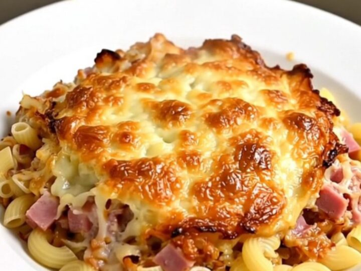 A close-up of a steaming portion of creamy elbow pasta with diced ham in a rich cheese sauce.