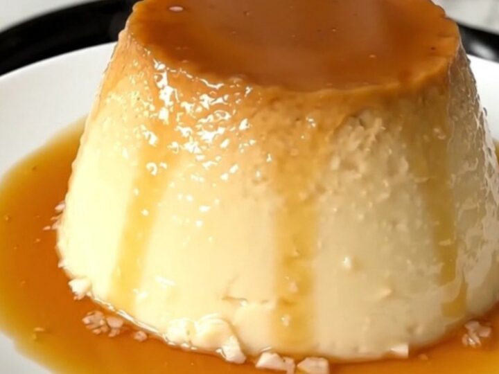 A finished coconut flan with a glossy caramel topping on a white plate.