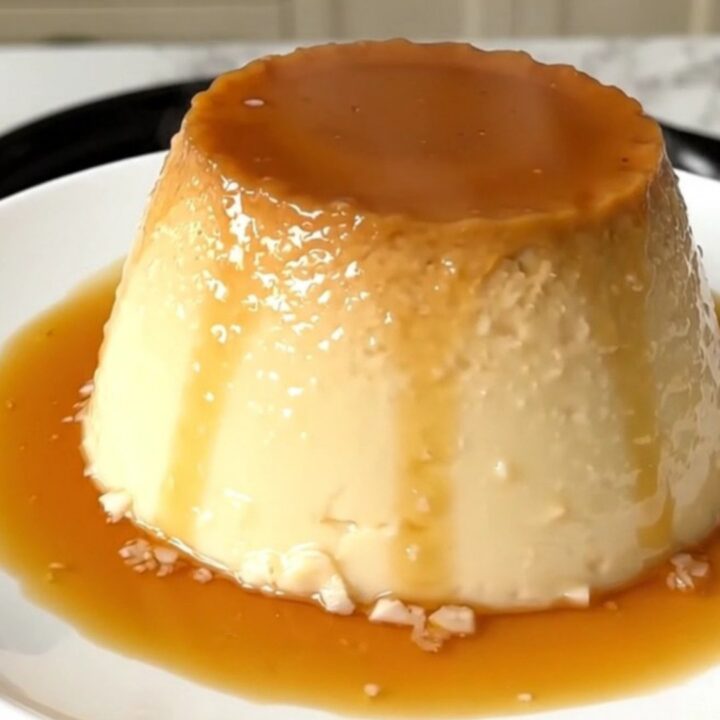 A finished coconut flan with a glossy caramel topping on a white plate.