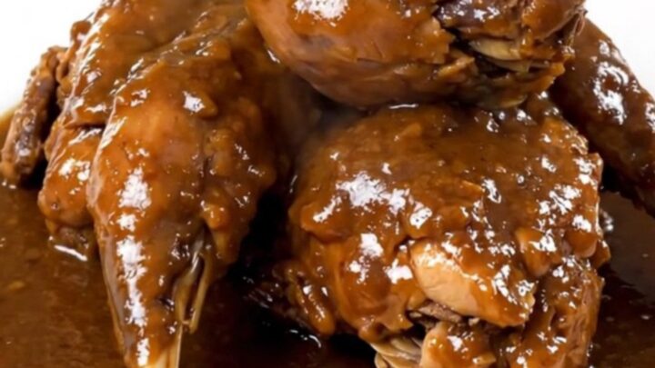 A close-up of tender, braised rabbit pieces coated in a glossy, dark beer sauce served on a white plate.
