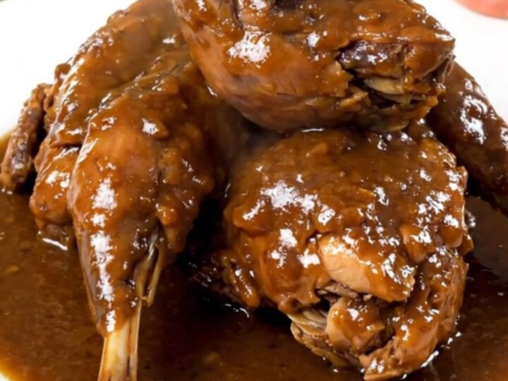 A close-up of tender, braised rabbit pieces coated in a glossy, dark beer sauce served on a white plate.