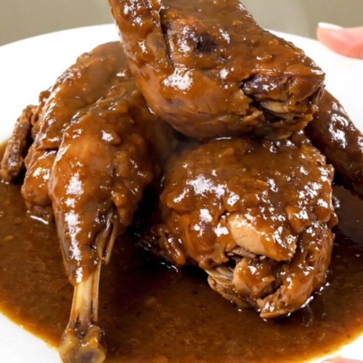 A close-up of tender, braised rabbit pieces coated in a glossy, dark beer sauce served on a white plate.
