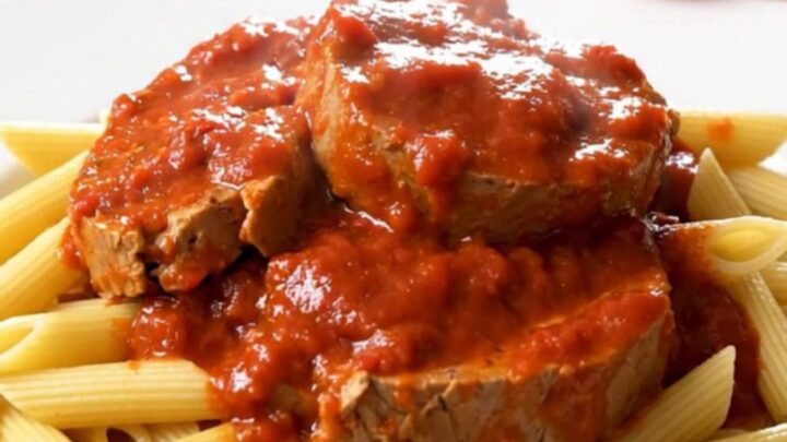 A top-down view of raw veal tendrons, sliced onions, and tomato coulis inside a black slow cooker insert.