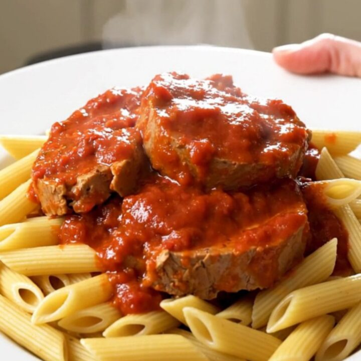 A top-down view of raw veal tendrons, sliced onions, and tomato coulis inside a black slow cooker insert.