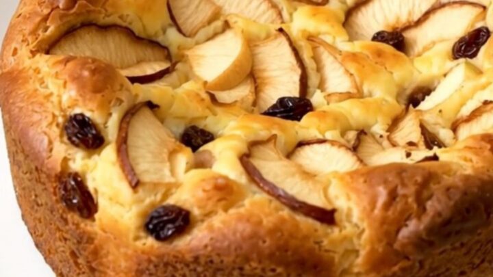 A warm, golden apple rum raisin clafoutis served on a white plate.