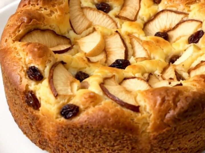A warm, golden apple rum raisin clafoutis served on a white plate.