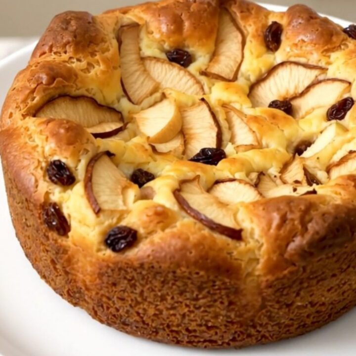 A warm, golden apple rum raisin clafoutis served on a white plate.