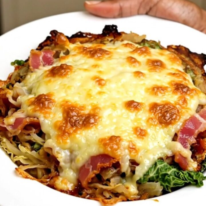 A slow cooker filled with creamy savoy cabbage, bacon, and melted Cantal cheese on a quartz countertop.