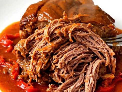A tender lamb shoulder served on a white plate with rich red pepper sauce.