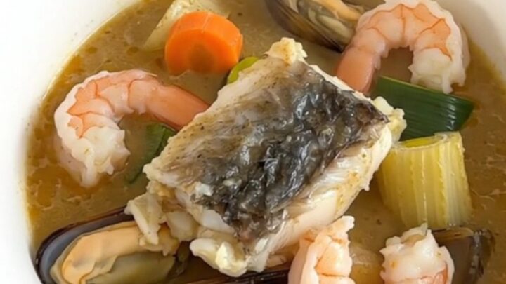A steaming, creamy seafood stew in a white bowl against cream-colored kitchen cabinets.