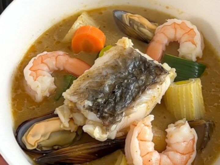 A steaming, creamy seafood stew in a white bowl against cream-colored kitchen cabinets.