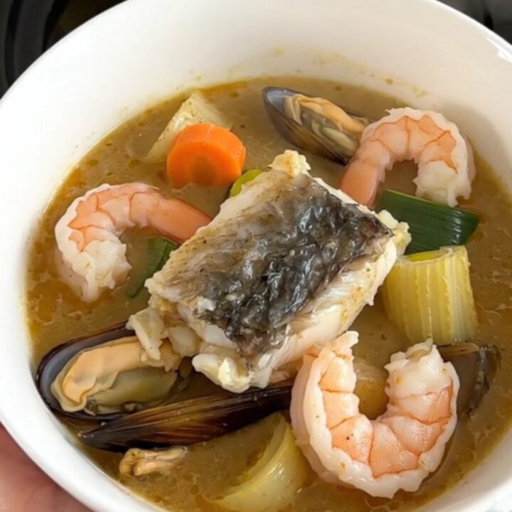 A steaming, creamy seafood stew in a white bowl against cream-colored kitchen cabinets.