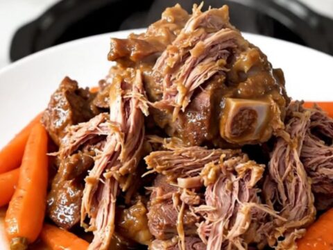 A succulent, slow-cooked veal shank served with tender carrots on a white plate.