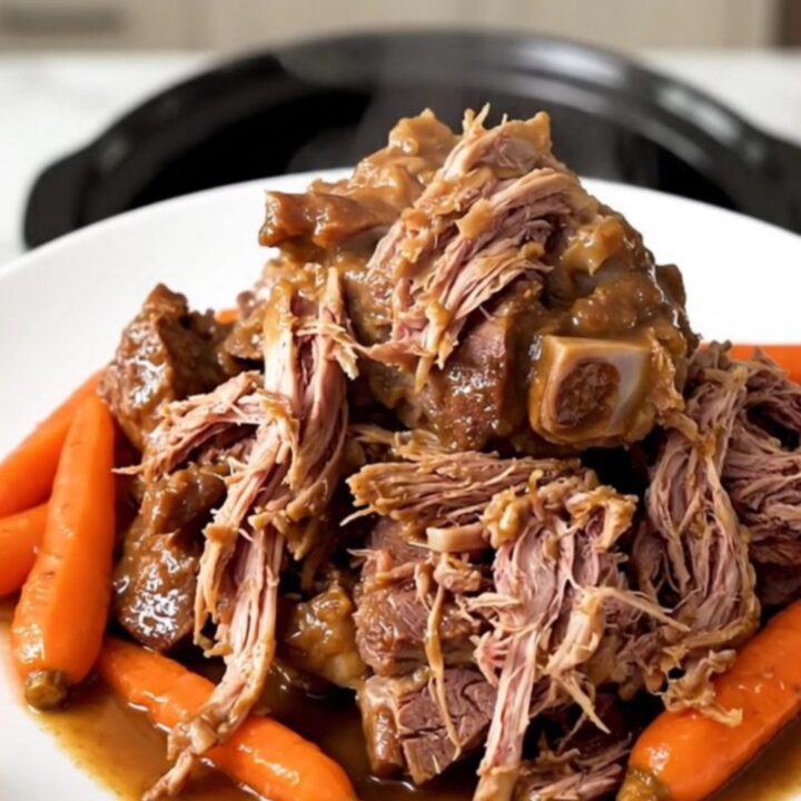 A succulent, slow-cooked veal shank served with tender carrots on a white plate.