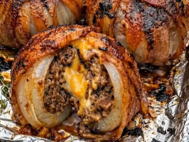 Five golden-brown, bacon-wrapped onion bombs served on a foil-lined baking sheet.