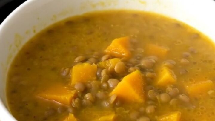 A rustic bowl of lentil and pumpkin soup steaming in a bright kitchen setting.