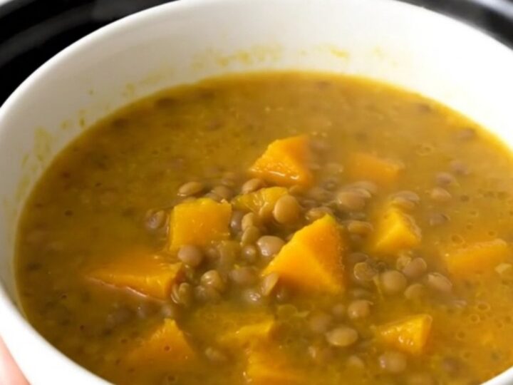 A rustic bowl of lentil and pumpkin soup steaming in a bright kitchen setting.